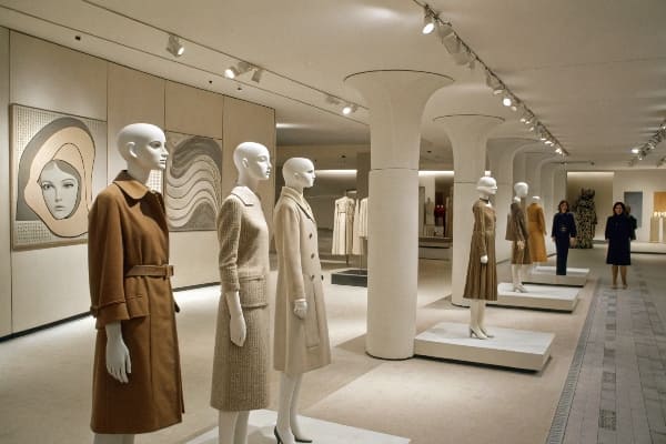Elequines elegantes en abrigos de tonos neutrales en una exhibición de moda estilo museo.
