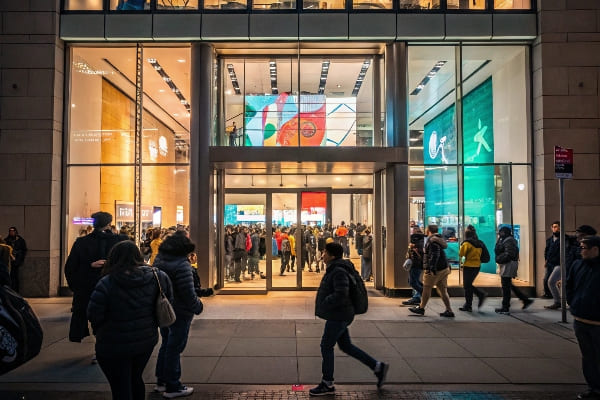 Entrada de la tienda llena de gente por la noche con pantallas interiores brillantes y tráfico peatonal.
