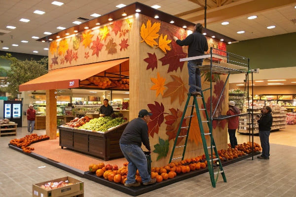 Los trabajadores que decoran la sección de productos con temática de otoño con calabazas y hojas de otoño.