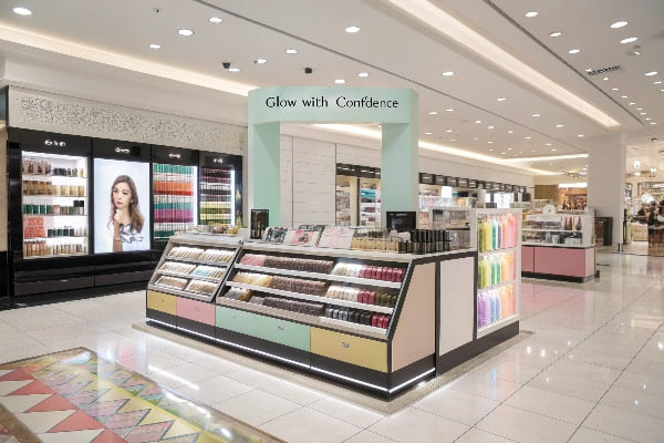 Exhibición de cosméticos en grandes almacenes con banner de 'Glow With Confidence'