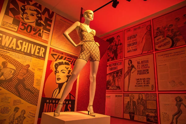 Mannequin estilizado en atuendo estampado bajo una dramática iluminación roja con carteles retro.