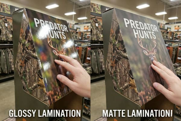 A side-by-side comparison of two retail display boxes for 'PREDATOR HUNTS', showcasing the difference between glossy and matte lamination finishes. The left box, labeled 'GLOSSY LAMINATION', reflects overhead store lights, highlighting its shiny surface and a hand touching a deer image. The right box, labeled 'MATTE LAMINATION', shows a non-reflective, smooth finish with a hand touching the same deer image, both set against a backdrop of camouflage hunting gear in a store.