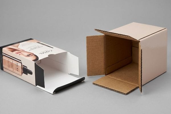 A non-corrugated folding carton featuring Bexy Coral cosmetic packaging lies beside an open corrugated box revealing its internal fluted structure.