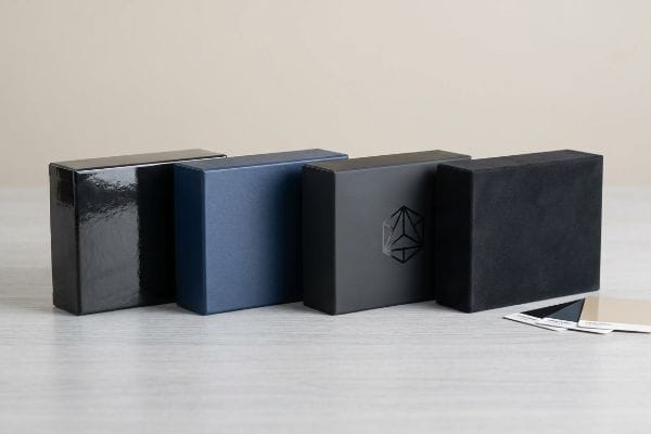 四个包装盒展示了不同的涂层：亮黑色、哑光海军蓝、带有几何标志的深灰色和带有色卡的柔触黑色。.