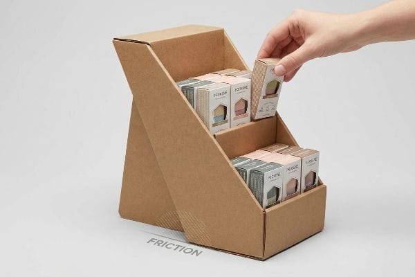 Brown corrugated cardboard two-tier countertop display filled with Prokine cosmetic boxes, a hand removing one, with 'Friction' graphic.