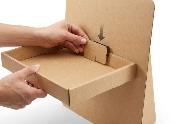 Corrugated cardboard modular tray being secured into a display board back panel, showing hands aligning the locking tab.