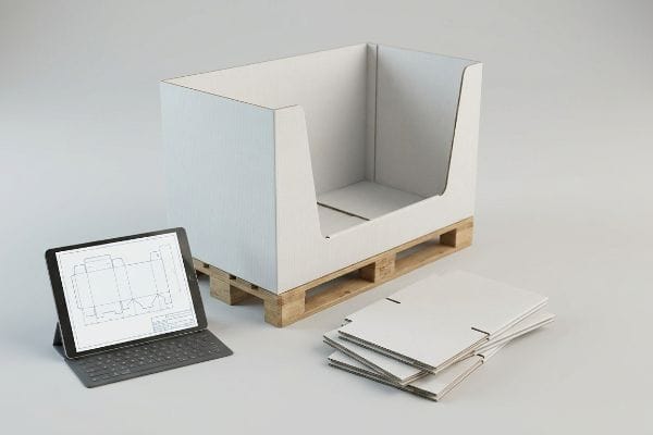An unprinted white corrugated cardboard pallet display sample on a wooden pallet, with a tablet showing structural dielines and flat-packed components, for testing assembly and logistics.