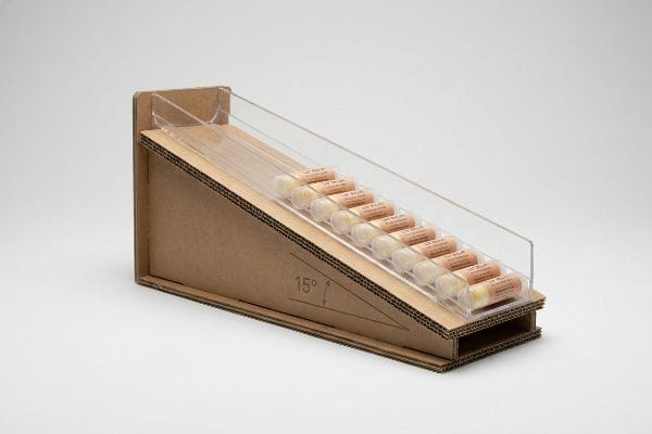 Corrugated cardboard and clear acrylic gravity feed display holding Lip Balm tubes at a 15-degree angle for auto-replenishment.