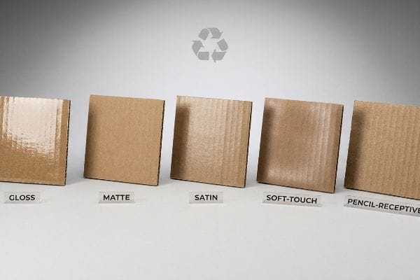 A row of five corrugated cardboard samples displays different aqueous coating finishes: Gloss, Matte, Satin, Soft-Touch, and Pencil-Receptive, highlighting their distinct textures.