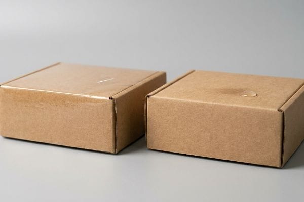 Brown corrugated cardboard boxes, one with a clear finish, the other showcasing water-resistant aqueous coating with a visible droplet.