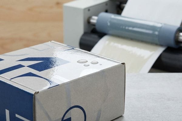 Glossy white and blue box with water droplets, showcasing water-resistant aqueous coating applied by a printing machine.