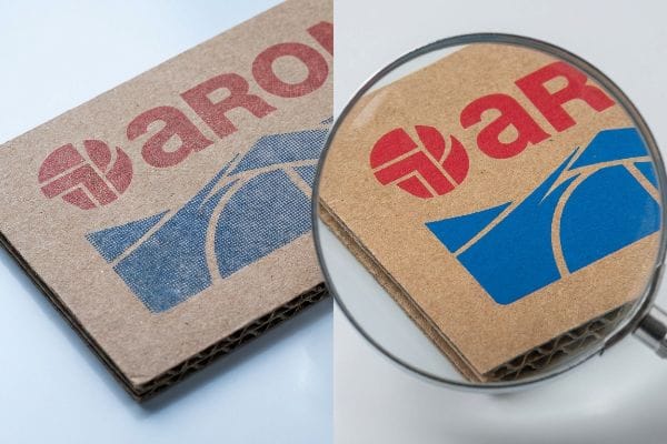 Brown corrugated board displays a red and blue Arox logo, revealing muddy halftone printing on porous fibers, magnified to show print texture and flutes.