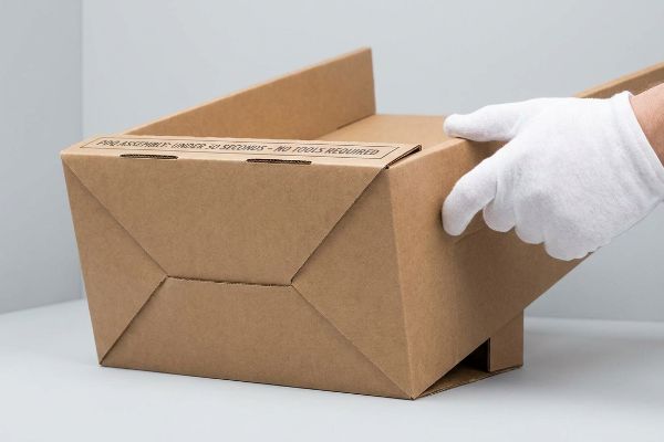 Brown corrugated PDQ display box with 'For Assembly Under 30 Seconds - No Tools Required' text, held by a white-gloved hand.