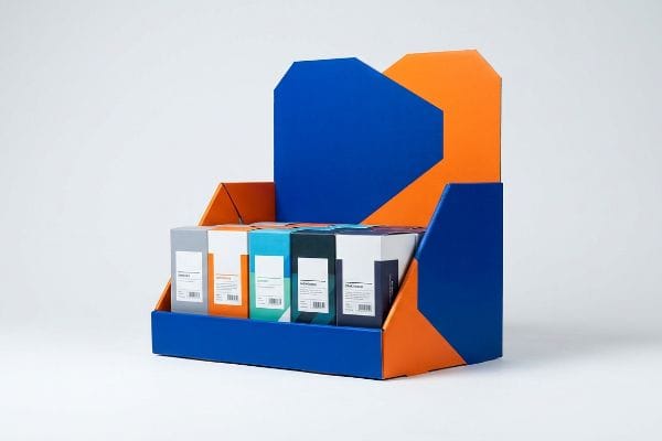 A vibrant blue and orange die-cut retail display stand holds five distinct product boxes, showcasing aggressive spatial engineering for impulse purchases.