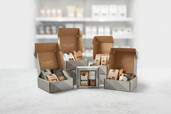 Several Brannen display packaging boxes, featuring gold foil branding and grey geometric patterns, showcase various packaged snacks and nuts on a retail floor.