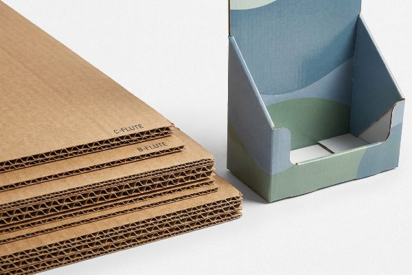 Corrugated cardboard sheets, C-Flute and B-Flute, are displayed alongside a printed countertop stand.