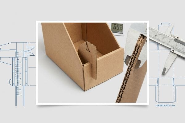 Caliper measuring corrugated B-flute thickness, alongside a display box, dieline blueprint showing 'Humidity Buffer +1mm', and 65% humidity.