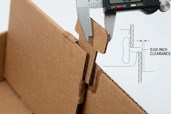 Digital caliper measuring 0.04 inch clearance between corrugated cardboard locking tabs, with diagram.