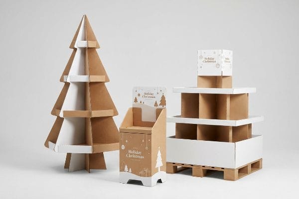 Brown kraft and white cardboard displays: a large Christmas tree floor model, a countertop POS unit, and a multi-tiered pallet display with 'Holiday Christmas' branding.