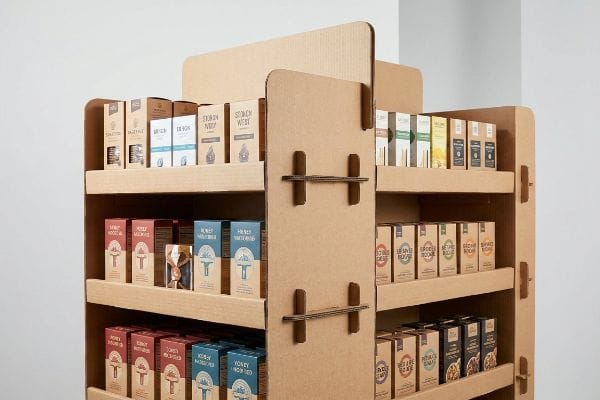 Corrugated cardboard endcap display with multiple shelves showcasing boxed 'Stoken West', 'Honey Milkwood', 'Doughnut', and 'Devon' products.