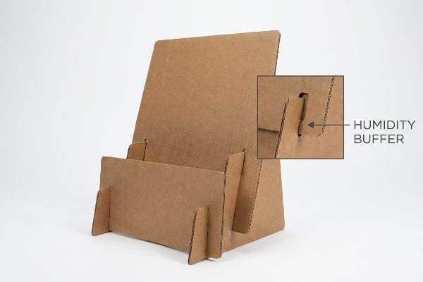 Brown corrugated cardboard display stand featuring a close-up of the Humidity Buffer slot, engineered for moisture resistance and frictionless assembly.