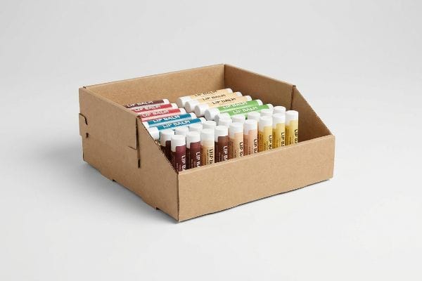 Brown corrugated cardboard PDQ display box filled with multi-colored Lip Balm tubes, ready for retail point-of-sale.