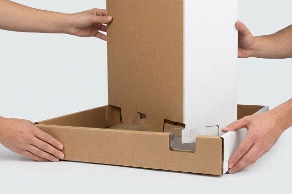 Hands assembling a brown cardboard pallet display base, featuring white modular trays and intuitive tab systems for easy setup.