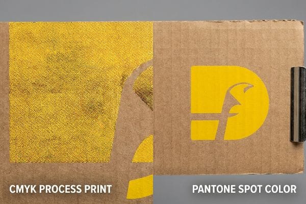 Close-up of corrugated board comparing grainy CMYK Process Print with solid, vibrant Pantone Spot Color yellow, highlighting halftone dots.