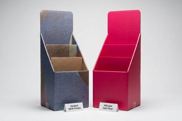 Corrugated cardboard display stands comparing grainy Standard CMYK Process print to vibrant PMS Spot Color Flood.