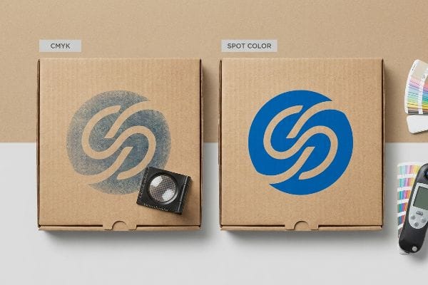 Corrugated cardboard boxes showcase a faded Cmyk halftone logo next to a vibrant Spot Color logo, illustrating print quality differences.