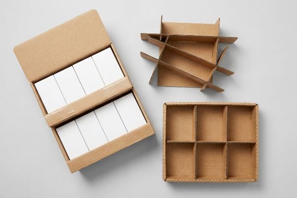Corrugated cardboard packaging components, featuring an open box with white products, a disassembled divider, and a 6-compartment retail-ready tray.