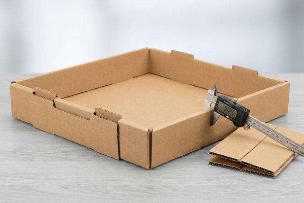 Brown corrugated cardboard display base with a digital caliper measuring 1.525mm thickness, demonstrating precise bend allowance for packaging.