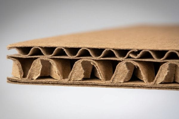 A close-up view reveals the intricate double-wall structure of brown corrugated cardboard, showcasing its two fluted layers and linerboards.