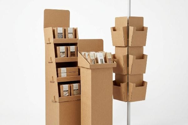 Affordable corrugated retail racks are displayed, featuring a tall floor stand, countertop tray, and modular sidekick unit.