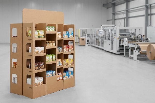 Corrugated cardboard display with shop-through architecture and windowed supports, holding food products in a packaging facility.