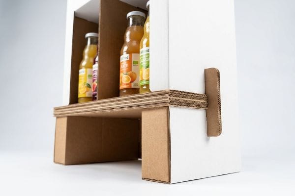 Corrugated cardboard beverage display with Valens orange, lemon, and berry juice bottles on a reinforced lower shelf, showcasing structural fluting.