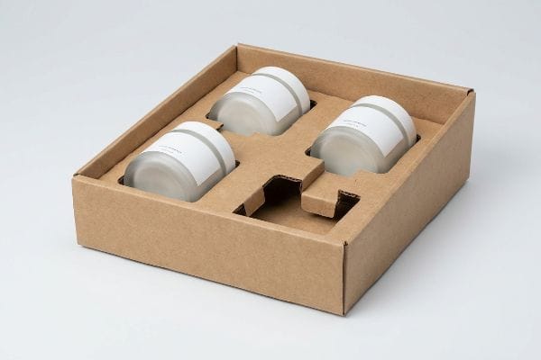 Brown corrugated cardboard packaging with a custom die-cut insert securely holding three frosted glass cosmetics jars with white labels.