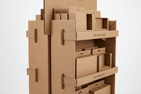 Sustainable corrugated cardboard toy display stand featuring '100% Recyclable' and 'Soy-Based Ink' text, with interlocking shelves and product cutouts.