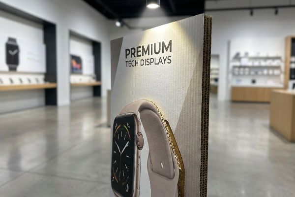 In einem Einzelhandelsgeschäft wird ein Aufsteller aus Wellpappe mit der Aufschrift „Premium Tech Displays“ präsentiert, der eine Smartwatch-Grafik und sichtbare Wellenform aufweist.