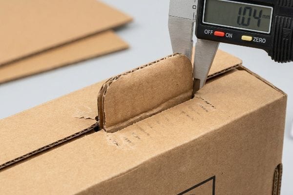 Digital caliper measures 1.04 mm thickness of a corrugated cardboard locking tab, crucial for humidity buffer.