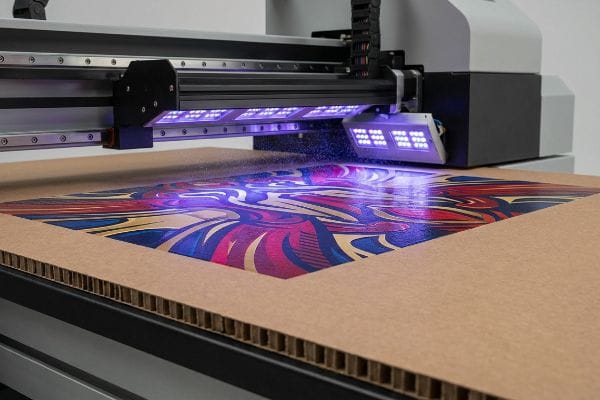 Corrugated cardboard receiving vibrant graphic print from a UV flatbed printer, showing instant ink polymerization under purple UV light.