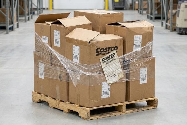 Brown cardboard boxes on a wooden pallet, wrapped in plastic film, featuring a Costco Wholesale Return Tag, ready for reverse logistics.