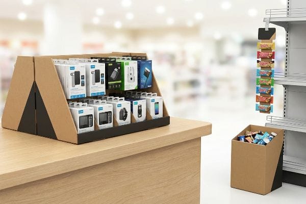 A retail checkout zone displays point-of-sale examples: a cardboard countertop merchandiser, a hanging clip strip with snacks, and a compact dump bin.
