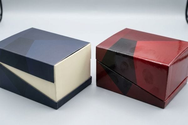Two glossy boxes, one dark blue and one dark red, display geometric patterns, emphasizing the direct reflection of gloss lamination.
