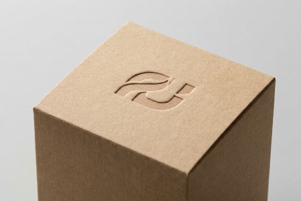 Light brown kraft paper box with a debossed abstract logo, showcasing premium tactile texture and elegant shadow contrast.