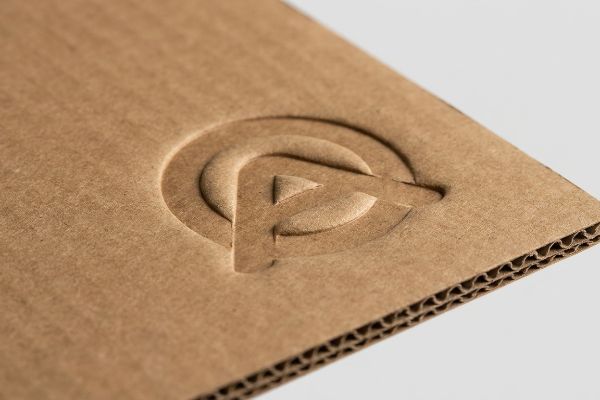 Brown corrugated cardboard displays a deep debossed logo, highlighting the kraft paper texture and visible flutes.