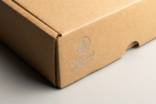 The side of a brown corrugated cardboard box features a silver 'Defond soy based ink' logo, highlighting eco-friendly packaging.