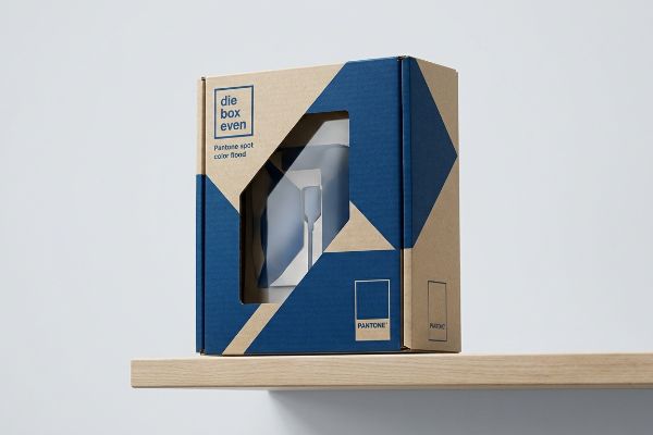 Embalaje de cartón Kraft con un patrón geométrico azul y ventana troquelada, que incluye