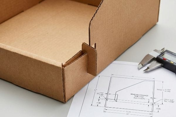 Corrugated cardboard box with interlocking tabs, beside a dieline drawing detailing