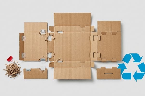 Brown corrugated cardboard box disassembled with metal clips, shredded paper, and a blue recycling symbol, illustrating mixed-material challenges.
